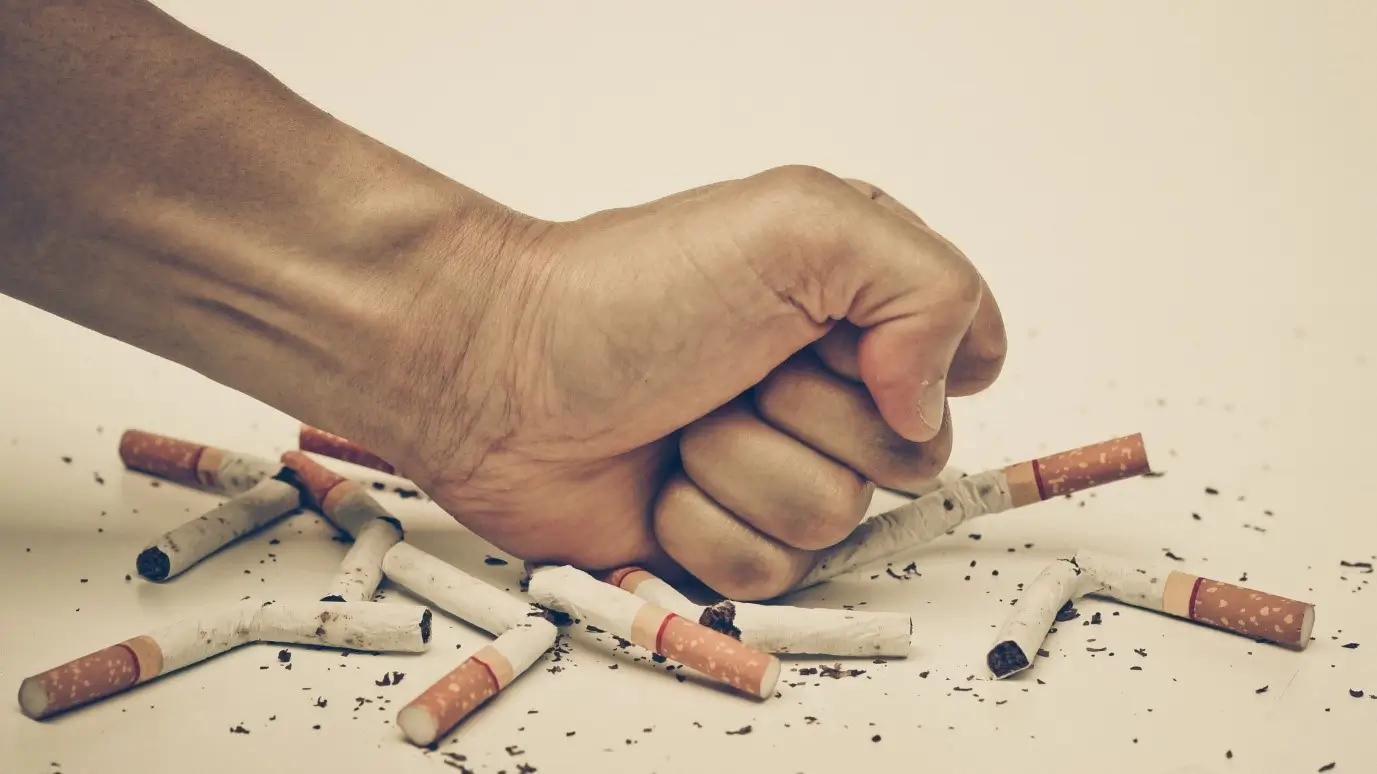 Hand crushing cigarettes to symbolize quitting smoking and the transition away from tobacco.